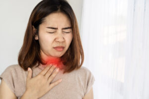 foto de uma mulher com muita dor de garganta, com a mão no pescoço em uma região pintada de vermelho, indicando dor