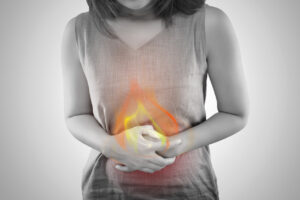foto em preto e branco de uma mulher com as duas mãos apertando sua barriga e uma chama acima, indicando incômodo e azia no estômago