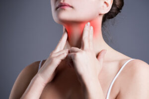foto do rosto de uma mulher com seus dois dedos apertando os cantos do próprio pescoço, coloridos em vermelho, para indicar a região da dor