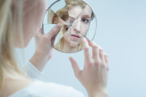 mulher olhando seu reflexo em um espelho quebrado